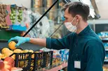 seller in a protective mask standing in front of the counter with fruit. coronavirus in the city