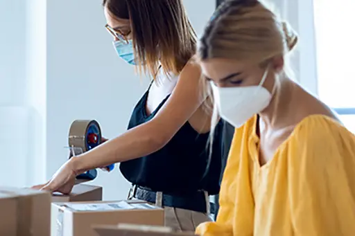 Shot of two beautiful freelance business women seller wearing a hygienic facial mask while checking product order while packing and sealing cardboard boxes in their startup small business.
