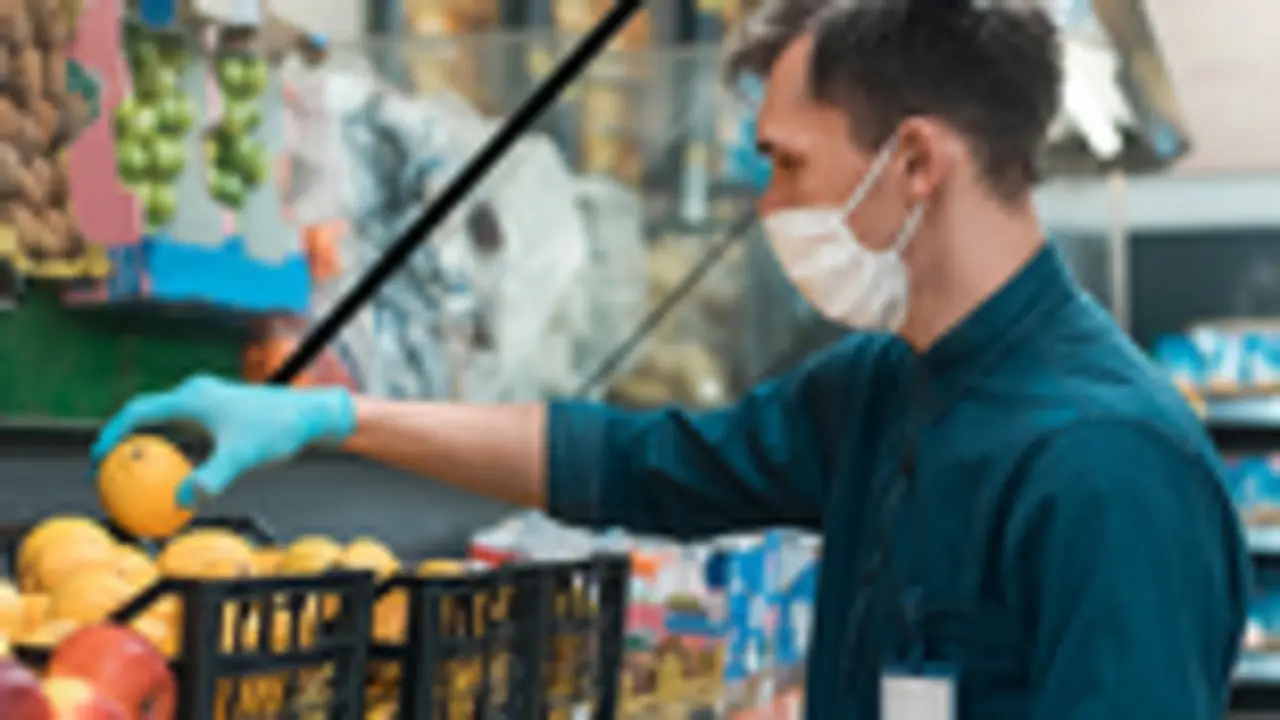 seller in a protective mask standing in front of the counter with fruit. coronavirus in the city