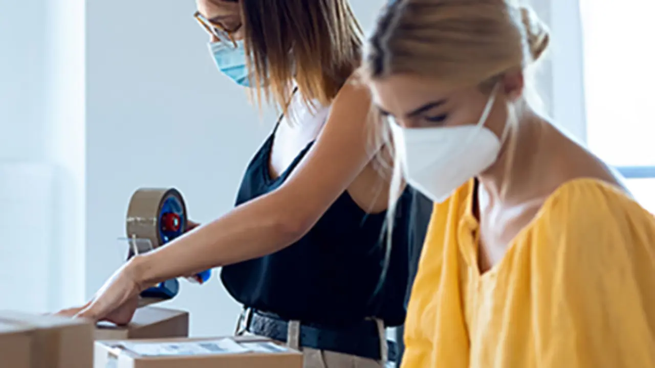Shot of two beautiful freelance business women seller wearing a hygienic facial mask while checking product order while packing and sealing cardboard boxes in their startup small business.