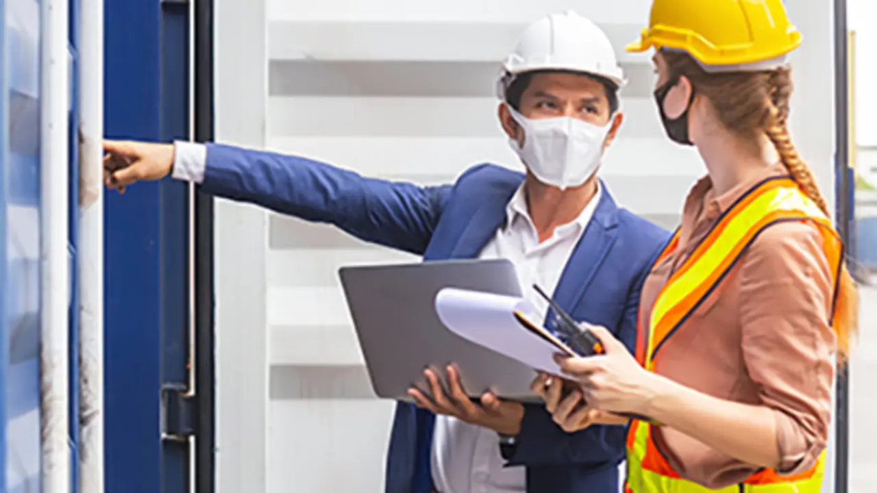 Teamwork foreman man and woman wearing protection face mask and safety helmet using laptop and holding clipboard checking containers in cargo ship for import export, Industrial container cargo concept.